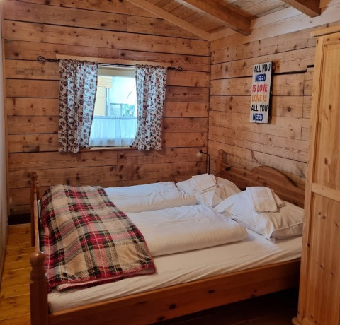 Dormitorio rústico de glamping con cama doble, manta a cuadros y cortinas florales en Glamping Bad Gastein.