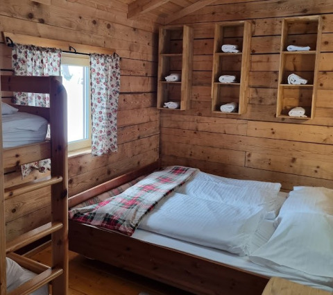 Houten kamer bij Glamping Bad Gastein met stapelbed, tweepersoonsbed, bloemen gordijnen en handdoeken.