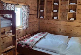 Chambre boisée avec lit superposé, grand lit, plaid écossais et serviettes roulées, Glamping Bad Gastein.