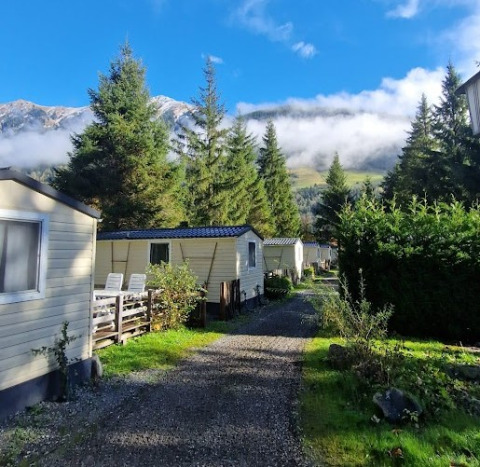 Glamping Bad Gastein - Kurcamping Erlengrund con case mobili, pini e vista sulle montagne sotto un cielo azzurro.