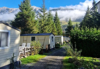 Glamping Bad Gastein - Kurcamping Erlengrund met stacaravans, dennenbomen en bergen onder een blauwe lucht.