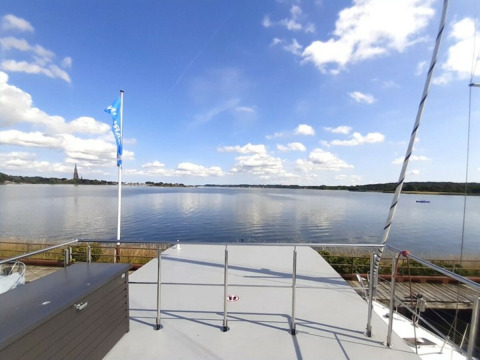 Blick von Wind & Wellen - Woontboot Sleeswijk-Holstein mit ruhigem Wasser, Himmel und Wolken.