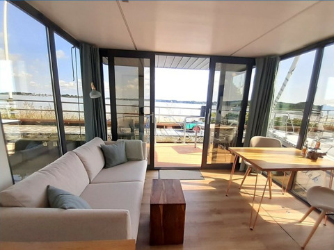 Helles Wohnzimmer mit Sofa, Tisch und Seeblick von Wind & Wellen - Woontboot in Schleswig-Holstein.
