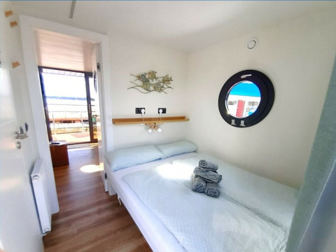 Bright, compact bedroom on Wind & Wellen houseboat in Sleeswijk-Holstein with porthole and outside view.