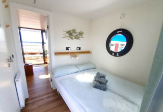 Helles Schlafzimmer auf dem Wind & Wellen Hausboot in Sleeswijk-Holstein mit Bullauge und Außenaussicht.