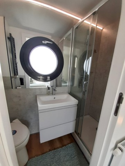 Moderne badkamer in glampingaccommodatie Wind & Wellen - Woontboot Schleswig-Holstein met rond raam.
