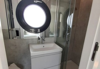 Salle de bains moderne dans un logement glamping Wind & Wellen - Woontboot Schleswig-Holstein avec hublot.