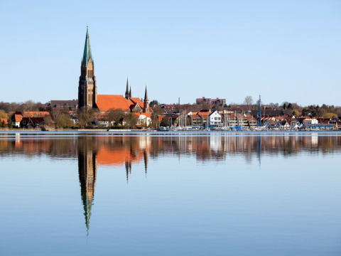 Stadtansicht mit Kirche, Booten und Spiegelung im Wasser in Schleswig vom Wind & Wellen - Woontboot Schleswig-Holstein aus.