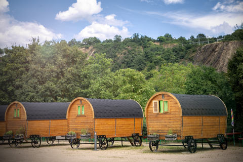 Drei Holzwagen zum Glamping im Camping Gülser Moselbogen - Herderwagens, Rheinland-Pfalz, bei Bäumen.