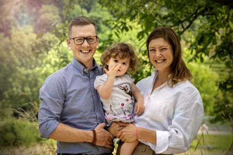 Una familia feliz posa en Camping Gülser Moselbogen - Herderwagens Rijnland-Palts, rodeada de naturaleza verde.