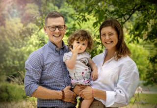 Une famille souriante pose à Camping Gülser Moselbogen - Herderwagens Rijnland-Palts, entourée de verdure.