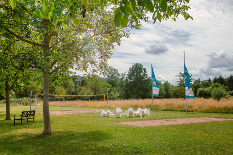 Outdoor view of Camping Gülser Moselbogen with volleyball court, chairs, flags, and green grassy area.