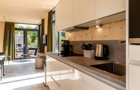 Moderne glampingbolig på UplandParcs Sauerland med tekøkken, store vinduer og grøn udsigt.