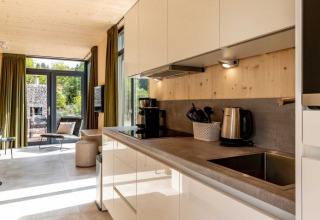 Hébergement glamping moderne à UplandParcs Sauerland avec cuisine, grandes fenêtres et vue sur la nature.
