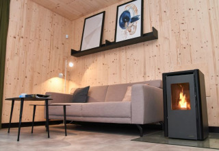 Sala moderna en UplandParcs Sauerland Wellness Cottage con sofá, paredes de madera y estufa de leña.