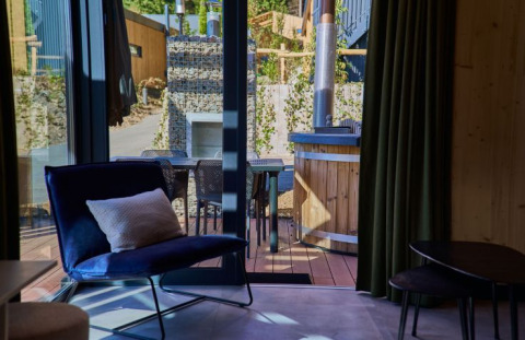 Interior de glamping en UplandParcs Sauerland Wellness Cottage, vista a la terraza y tina de madera afuera.