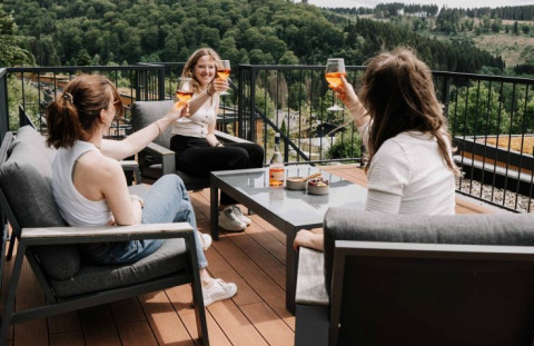 Tres mujeres brindan con bebidas en la terraza de UplandParcs Sauerland Wellness Cottage con vistas a la naturaleza.