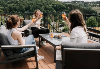 Drei Frauen stoßen mit Getränken auf der Terrasse des UplandParcs Sauerland Wellness Cottage im Grünen an.