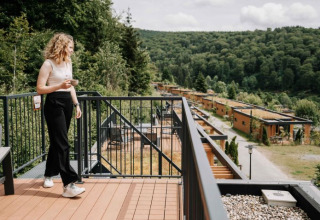 Donna beve caffè sul balcone di UplandParcs Sauerland Wellness Cottage con vista sulle colline verdi.