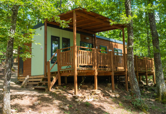 Modern cottage with wooden terrace at Chianti Glamping Resort, surrounded by trees, perfect for glamping.
