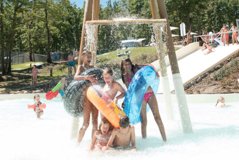 Niños juegan bajo una cascada de agua en el parque acuático de Chianti Glamping Resort rodeados de naturaleza.