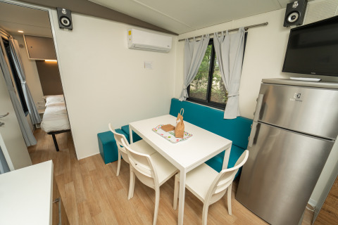 Intérieur d’un cottage moderne du Chianti Glamping Resort avec table à manger, réfrigérateur et chambre.