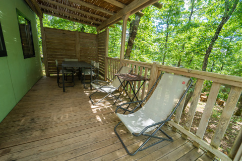 Terraza de madera con sillas y mesa en Chianti Glamping Resort, rodeada de árboles verdes en la Toscana.