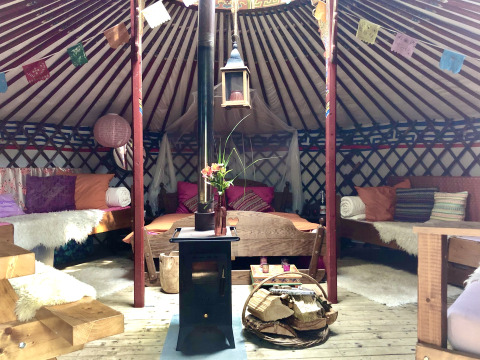 Gemütliche Yurt-Innenansicht mit farbigen Kissen, Ofen und Holzdetails bei Glamping 't Buitenland - Yurts Brabant.