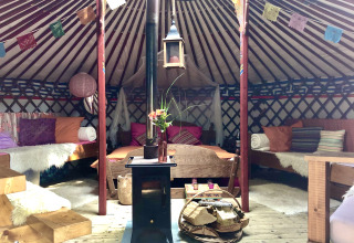 Interior de yurt acogedor con cojines coloridos, muebles y estufa en Glamping 't Buitenland - Yurts Brabant.