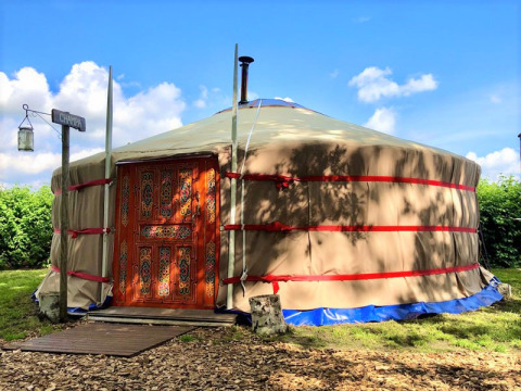 Glamping-yurt met kleurrijke deur bij Glamping 't Buitenland - Yurts Brabant onder een blauwe lucht.