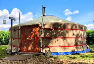 Yourte de glamping à porte décorée chez Glamping 't Buitenland - Yurts Brabant sous un ciel ensoleillé.
