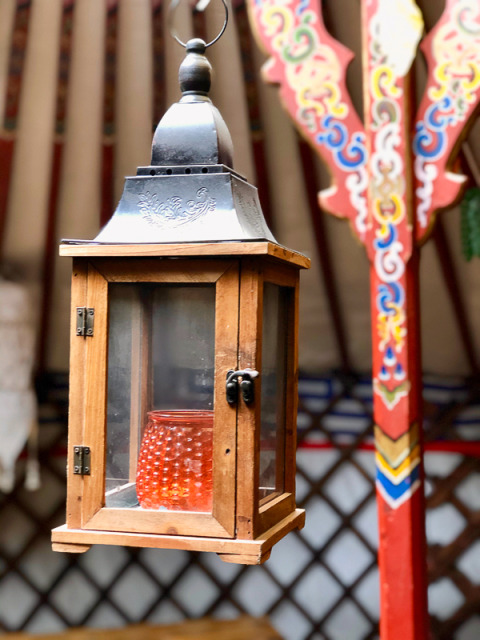 Holzlaterne mit Glaseinsätzen und rotem Licht innen, aufgehängt in einer kunstvoll bemalten Yurt.
