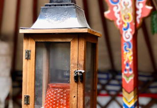 Lanterne en bois avec vitres et bougie rouge à l’intérieur, suspendue dans une yourte joliment décorée.