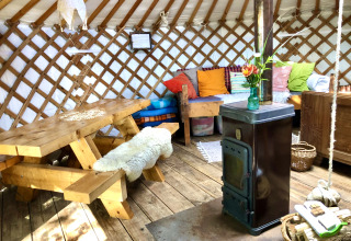 Interieur van een yurt met houten tafel, kleurrijke kussens, houtkachel en een gezellige sfeer.