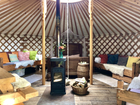 Knusse yurt-interieur bij Glamping 't Buitenland met houtkachel, kleurrijke kussens en houten banken.