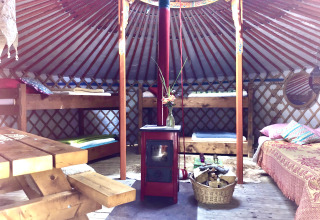 Interno di una yurta con letti a castello, tavolo in legno, stufa e arredo accogliente per glamping.