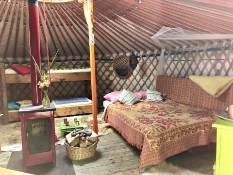Intérieur chaleureux d'une yourte chez Glamping 't Buitenland avec lit double, lits superposés et poêle à bois.
