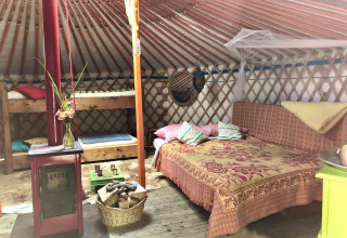 Cozy yurt interior at Glamping 't Buitenland with double bed, bunk beds, wood stove, and rustic decor.
