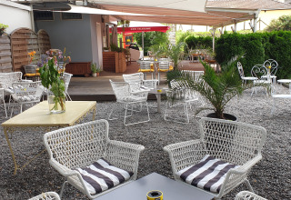 Buitenlounge van Camping Bellinzona met witte stoelen, planten, grind en zicht op de bergen.