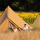 To personer nyder glamping foran telte med en mark af solsikker i baggrunden en solrig dag.
