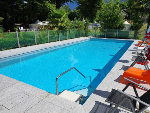 Piscina al aire libre con tumbonas en Camping Bellinzona - Mongoolse Yurt Suiza, rodeada de naturaleza.