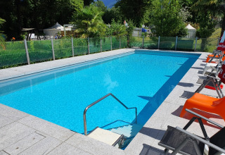 Piscina al aire libre con tumbonas en Camping Bellinzona - Mongoolse Yurt Suiza, rodeada de naturaleza.