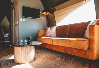 Interieur van een luxe glamping lodgetent bij Camping De Bovenberg, met comfortabele bank en moderne inrichting.