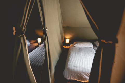 Binnenkant van een comfortabele glamping-lodgetent met bed en lampen, Camping De Bovenberg – Lodgetenten Twente.