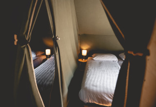 Interior de una tienda glamping acogedora con cama doble y lámparas en Camping De Bovenberg – Lodgetenten Twente.