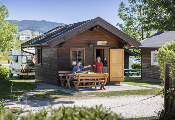 Dos personas disfrutan del desayuno frente a una cabaña de madera en Camp MondSeeLand, Austria, entre naturaleza.