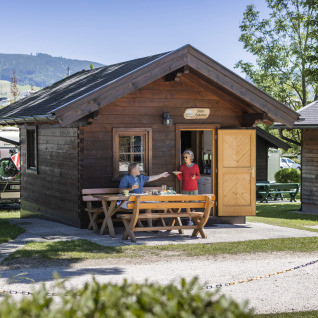 Deux personnes prennent le petit-déjeuner devant un chalet en bois au Camp MondSeeLand en Autriche, verdoyant.