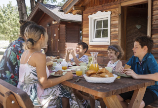 Family enjoys breakfast on a wooden table outside a cabin at Camp MondSeeLand - Kampeerhutten Austria.