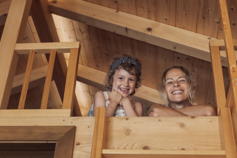 Twee personen glimlachen en kijken naar beneden vanuit een houten hut bij Camp MondSeeLand, Oostenrijk, glamping.