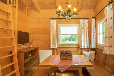 Acogedora cabaña de madera con mesa de comedor, ventanas, televisor y cortinas en Camp MondSeeLand.